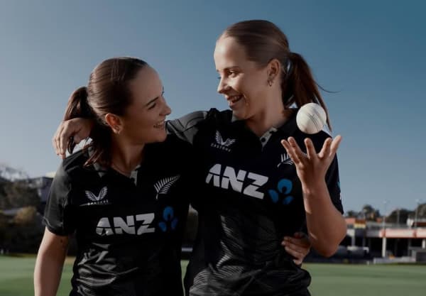Two brown-haired women with long ponytails smile at each other.