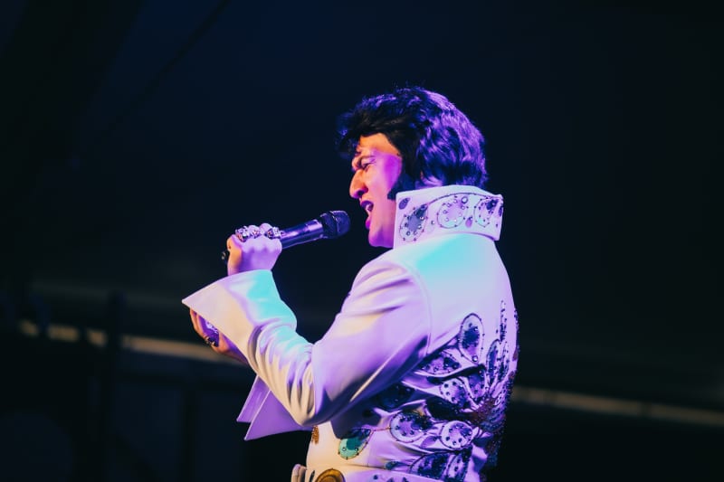 Taurean Kenny Mill holds a microphone as he performs on stage in full Elvis Presley attire.