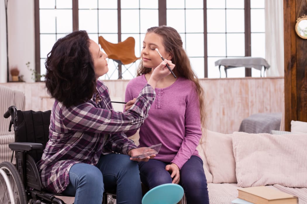 A photo of a woman in a wheelchair applying makeup on girl