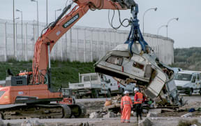 Workers watch as a crane destroys a caravan, once used as a makeshift shelter, at the site of the "jungle" migrant camp in Calais, northern France.