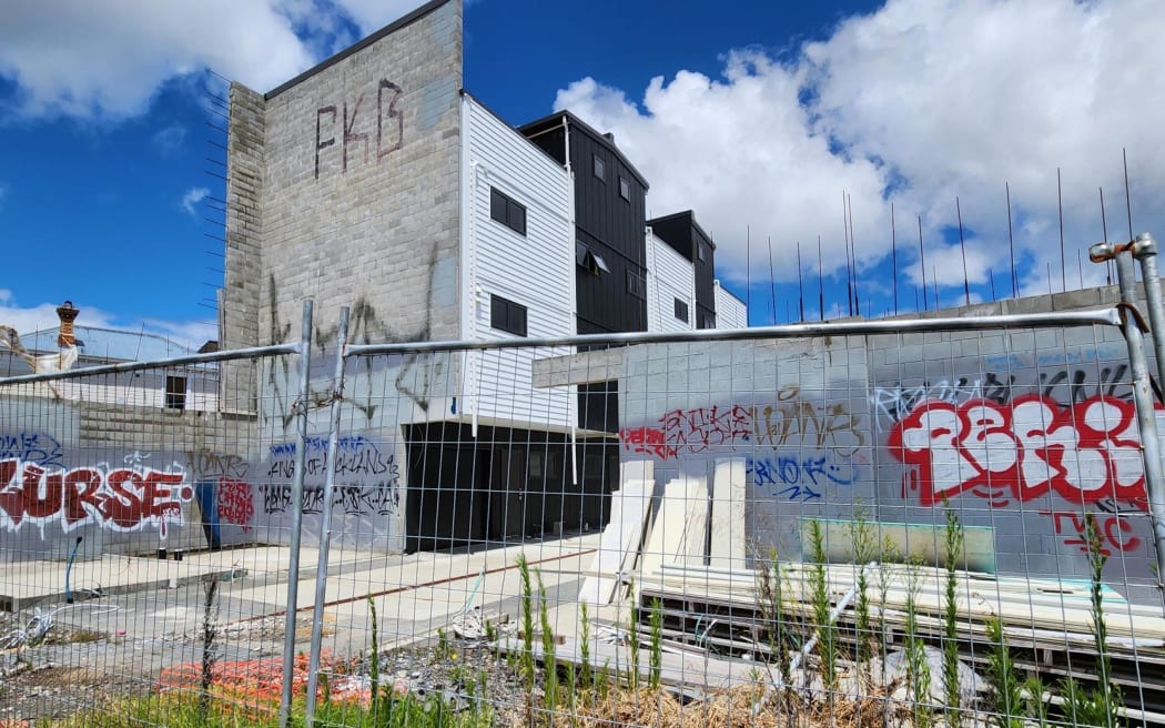 Half built townhouses surrounded by tagging and wonky fencing and overgrown grass on New North Rd.