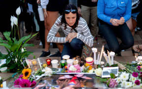 A woman kneels next to candles and flowers near a photo of murdered British backpacker Grace Millane during the vigil for murdered British backpacker Grace Millane at Civic Square Park in Wellington