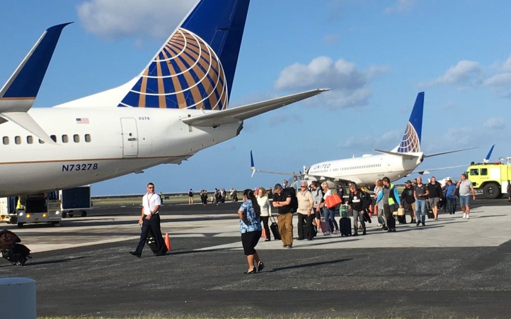 Passengers and flight crew who slept on a grounded United Airlines plane (rear) because of a Marshall Islands Covid-19 ban on incoming travelers deplane and walk to a rescue flight that arrived
Majuro shortly before 8am to collect the 124 passengers and flight crew.