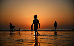 A child walks along the water’s edge at sunset at Scheveningen Beach in The Hague, Netherlands, on August 12, 2025. Amid a nationwide heatwave and a code yellow warning from the Royal Netherlands Meteorological Institute, thousands sought relief by the sea. (Photo by Mouneb Taim / Middle East Images via AFP)