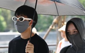 People shelter from the sun under an umbrella after visiting the Forbidden City during a heatwave in Beijing on June 24, 2023. Beijing recorded its third consecutive day of 40 degree Celsius weather, the first time since records began. (Photo by GREG BAKER / AFP)