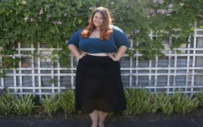 A portrait of Meagn Kerr standing in front of a garden wearing a black skirt and green crop top.