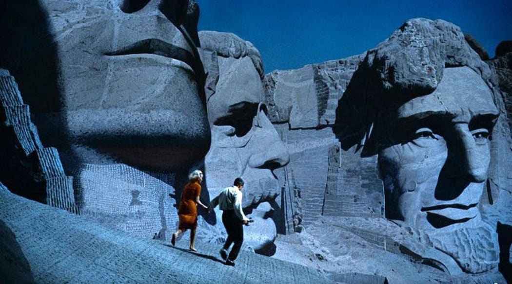 Movie still from Alfred Hitchcock's 1959 film North by Northwest featuring Eva Marie Saint and Cary Grant being pursued across Mt. Rushmore.
