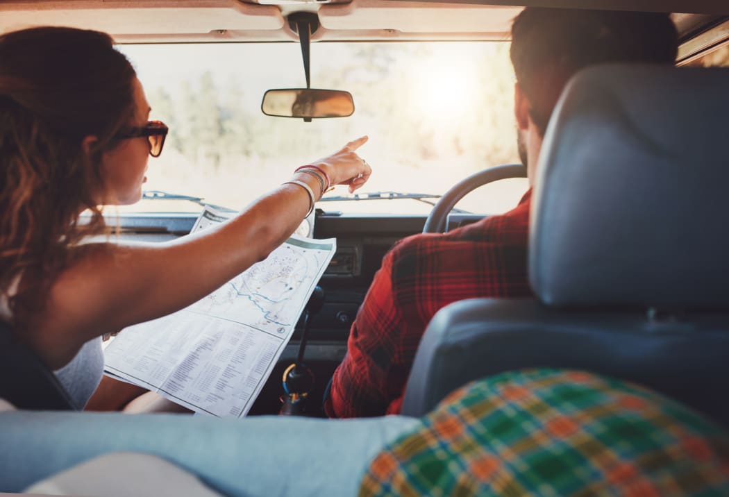 Passenger holding map and showing the route map to driver on road trip.