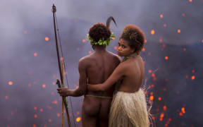 A man and a woman in traditional Ni-Vanuatu dress stand near the mouth of of an erupting volcano
