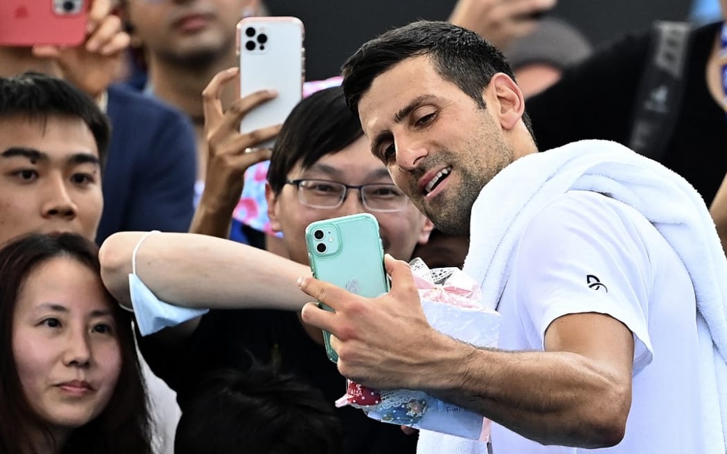Serbia's Novak Djokovic takes selfies with fans after a practice session on day two of the Australian Open tennis tournament in Melbourne on January 17, 2023. (Photo by MANAN VATSYAYANA / AFP) / -- IMAGE RESTRICTED TO EDITORIAL USE - STRICTLY NO COMMERCIAL USE --