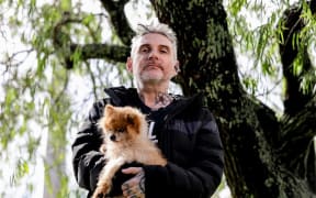 Author Dominic Hoey holding Pomeranian rescue dog, Chilli, in his arms as they stroll the streets of Grey Lynn, Auckland, where his new book, 1985 is set.
