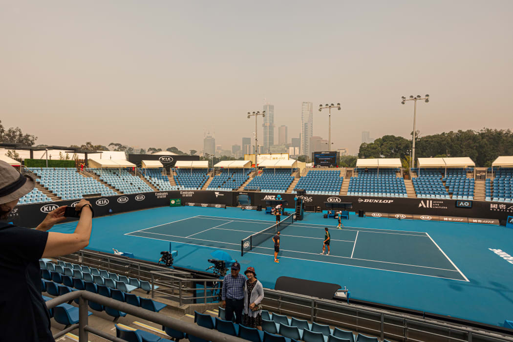 Tourists pose for a photo in the stands of one of the outside courts at Melbourne Park as the horizon is covered with thick smoke haze in Melbourne on January 15, 2020, ahead of the Australian Open tennis tournament.