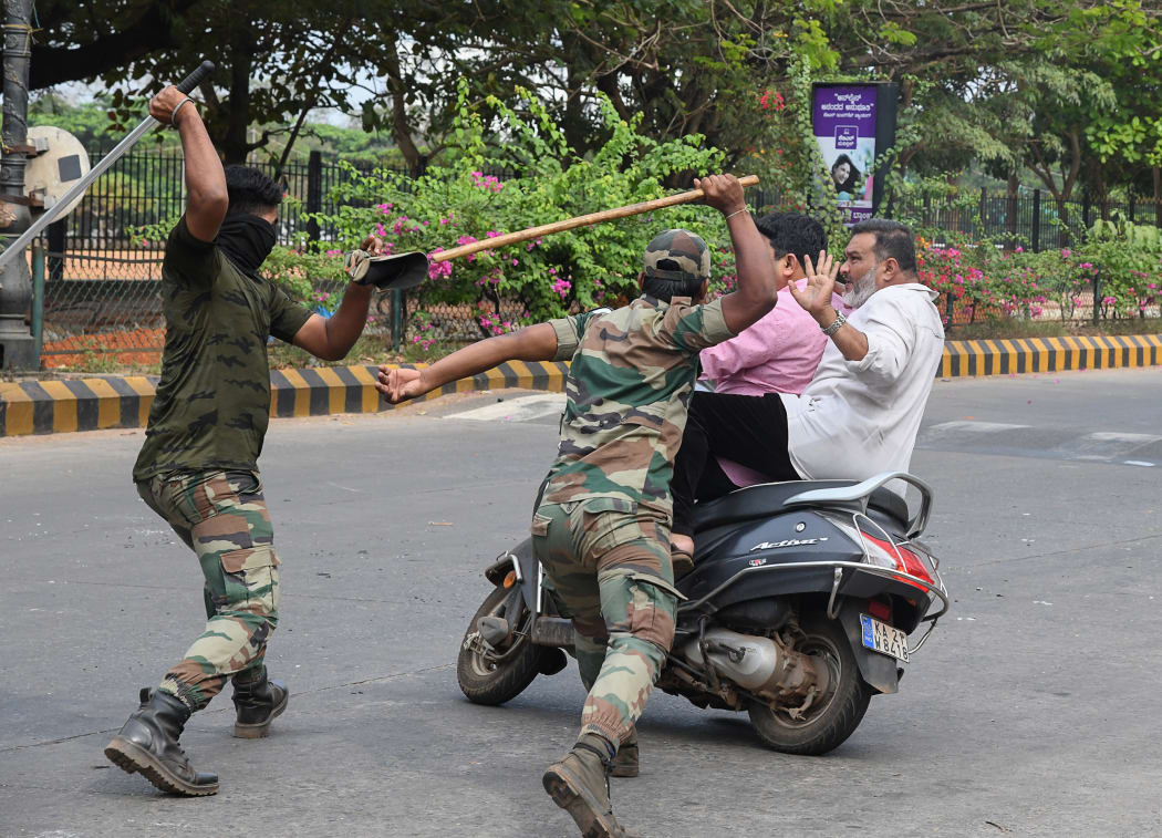 Members of the Karnataka Reserve Police Force swing their sticks to beat two men on a scooter who rode too close to a barricade set up on a street in Mangalore on December 20, 2019, amid heightened security due to protests over Indias new citizenship law.