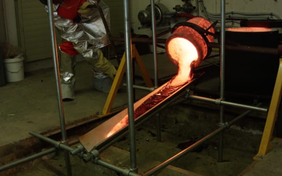 Molten lava pouring out the crucible down the tilted metal plate and beginning to cool down.