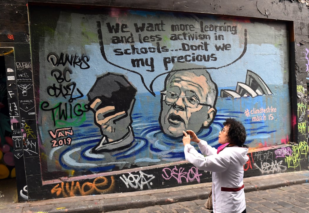 A tourist photographs a mural showing Australian Prime Minister Scott Morrison, who famously held up a chunk of coal and praised its value to Australia in a parliamentary debate on renewable energy in 2017.
