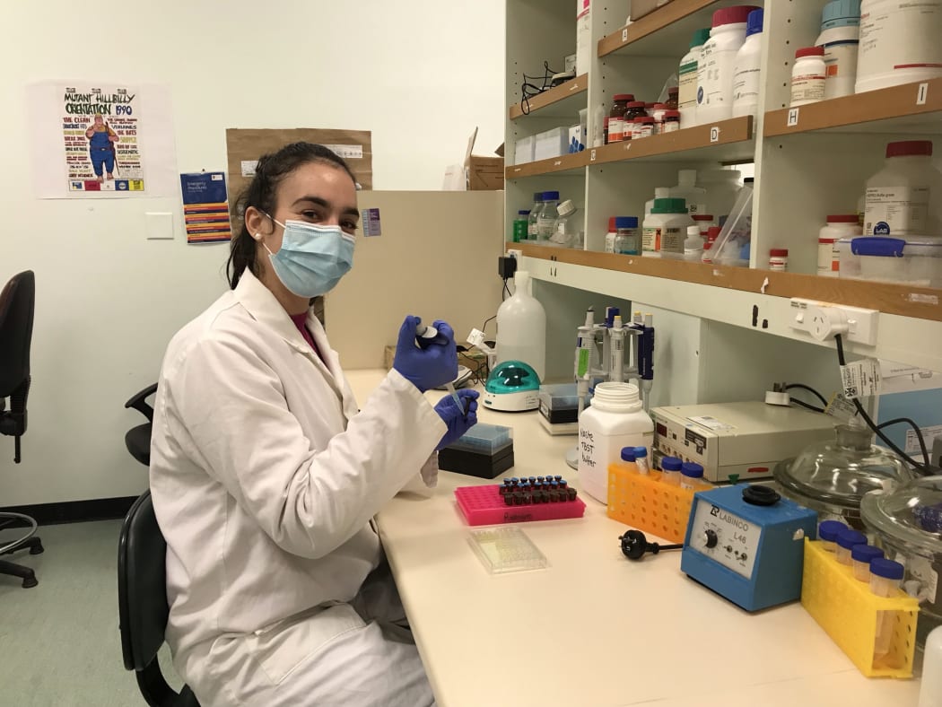 Lucy sits at a lab bench with a pipette in hand. There is a tray of small tubes in front of her as well as an array of different lab equipment.