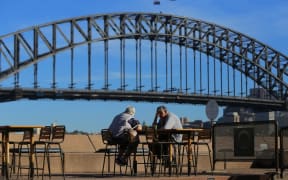 SYDNEY, AUSTRALIA - MARCH 19: An elderly couple sit at a table in front of the Sydney Harbour Bridge, following an outbreak of coronavirus (COVID-19), in Sydney, Australia.