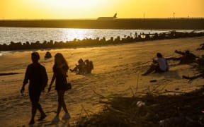 A plane lands at Ngurah Rai international airport as people watch sunset in Kelan Beach, Badung Regency, Bali, Indonesia, on 22 May 2023.