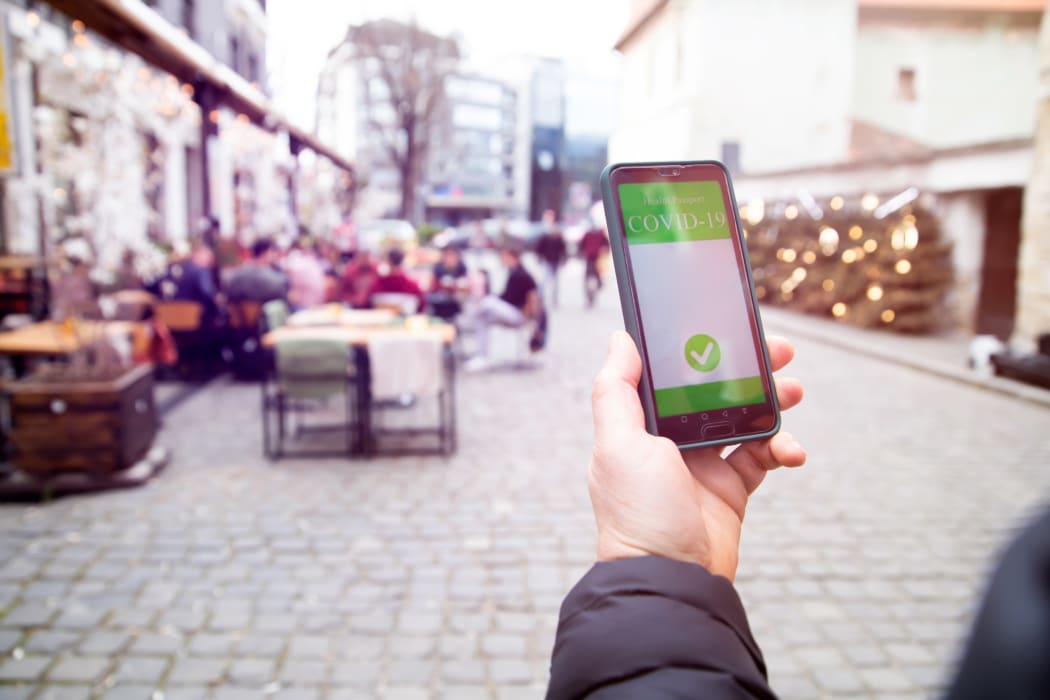 Vaccinated person using a digital vaccination or immunisation certificate on a smartphone at a restaurant terrace.