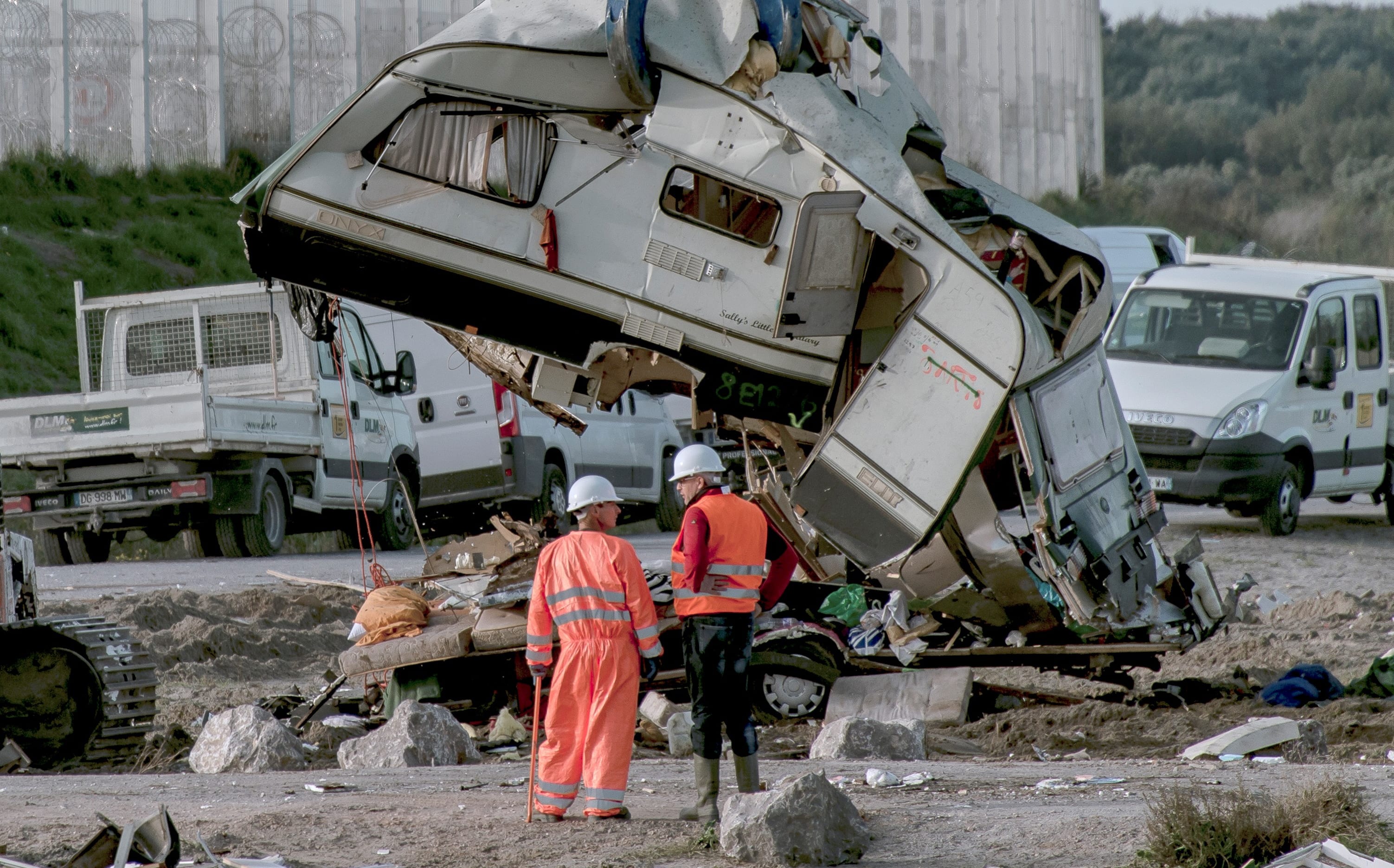 Workers watch as a crane destroys a caravan, once used as a makeshift shelter, at the site of the "jungle" migrant camp in Calais, northern France.