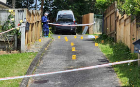 A driveway has been cordoned off by white and red police tape. It looks to be a suburban area and little yellow markers have been placed in the driveway.