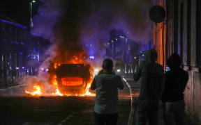A vehicle is set alight during an anti-immigration demonstration in Ballymena, Northern Ireland, on June 10, 2025. Violence flared for a second night June 10 in the Northern Irish town of Ballymena after "racially motivated" attacks sparked by the arrest of two teenagers accused of the attempted rape of a young girl. Hundreds of protestors, many of them masked, took to the streets of Ballymena, throwing petrol bombs and masonry as police responded with water cannon, an AFP journalist said. (Photo by PAUL FAITH / AFP)