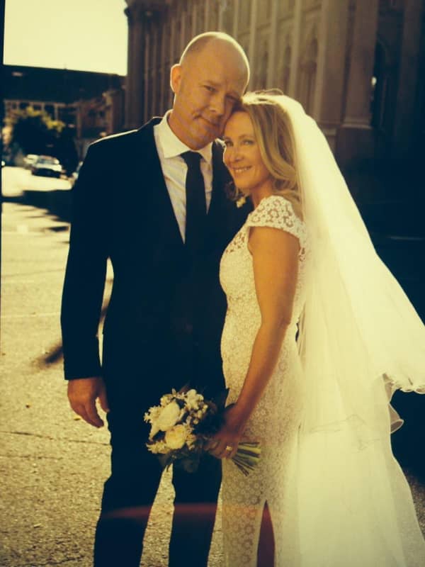 A couple in wedding attire smile slightly while standing in golden light.