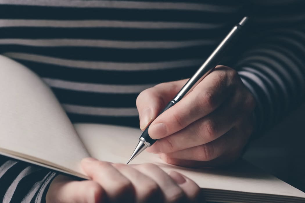 Left-handed woman writing diary, close-up of hands with pencil and notebook. (Photo by IGOR STEVANOVIC / SCIENCE PHOTO / IST / Science Photo Library via AFP)