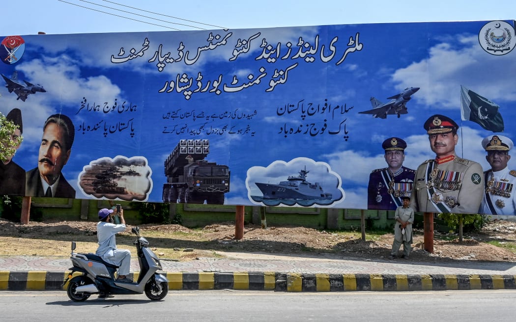 A man clicks a picture of a billboard featuring Pakistan's Army Chief General Syed Asim Munir (C), Naval Chief Admiral Naveed Ashraf (R), and Air Chief Marshal Zaheer Ahmed Babar Sidhu, along a road in Peshawar