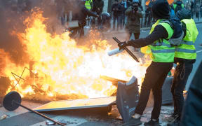 Two Gilet Jaune near a barricade on fire near the Gare Saint-Lazare on December 8, 2018 in Paris, France.