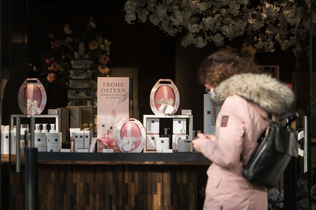A woman with protective face mask waits in front of store with the lettering "Happy Easter" in Berlin on 24 March 2021.