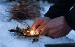 Man lighting a fire in a dark winter forest, preparing for an overnight sleep in nature, warming himself with DIY fire. Adventure, scouting, survival concept.