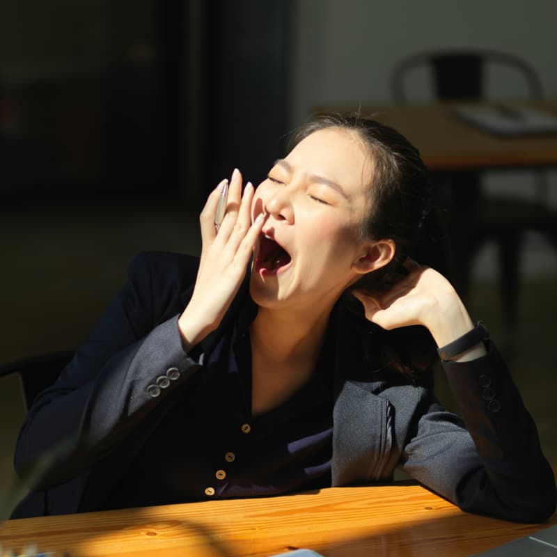 An Asian woman yawning at her desk.