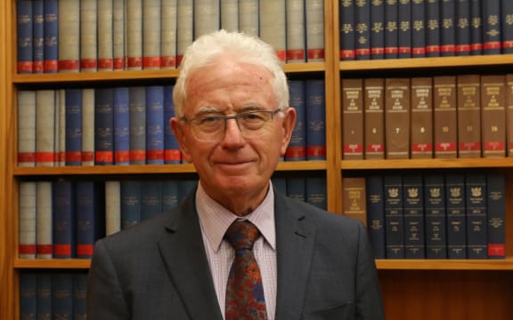 Sir Michael Cullen poses in the Labour Caucus Room in front of a bookcase of Hansard's verbatim reports of Parliament.