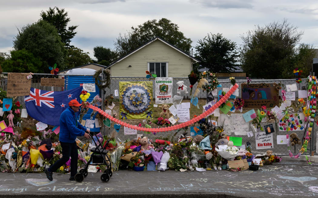 A man man walks past flowers and tributes displayed in memory of the twin mosque massacre victims along the road outside the Linwood mosque (back C) in Christchurch on March 25, 2019. The slaughter of 50 people at Friday prayers in two Christchurch mosques on March 15 shocked the normally laid-back country and prompted global horror, heightened by the gunman's cold-blooded livestreaming of the massacre. (Photo by ANTHONY WALLACE / AFP)