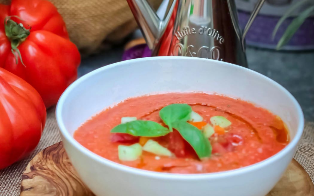 A white bowl of vibrantly red gazpacho decorated with fresh basil.