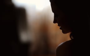 A young woman stands in silhouette against a window.