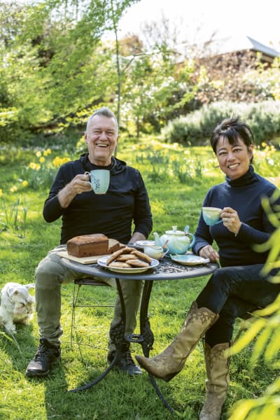 Jimmy and Jane Barnes sit with cups of tea and slices of cake at a table in their garden.