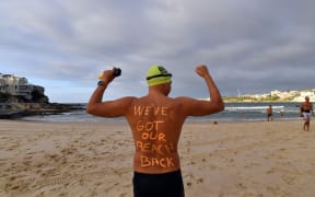 A man poses with a message on his back before enjoying his first swim after Bondi Beach reopened following a five week closure in Sydney on April 28, 2020.