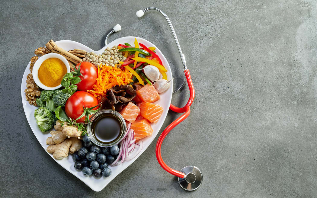 Fresh food for a healthy heart with acai, lentils, soy sauce, ginger, salmon, carrot, tomato, turmeric, cinnamon, walnuts, garlic, peppers, broccoli, basil, onion with a stethoscope and copy space