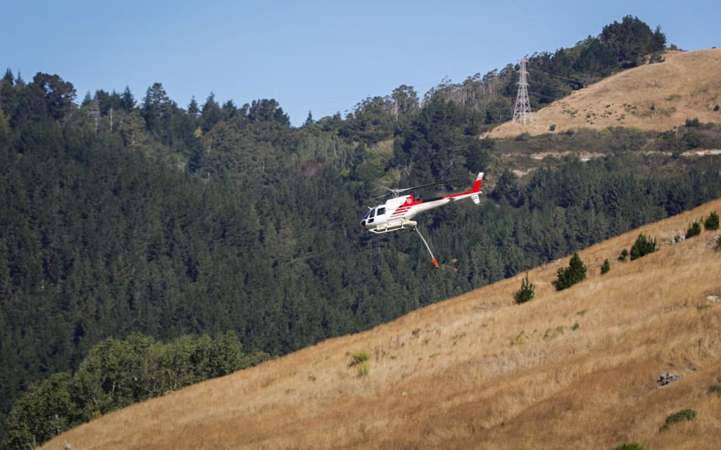 Helicopters fill their monsoon buckets to fight the blaze n the Port Hills, 14 February 2024.