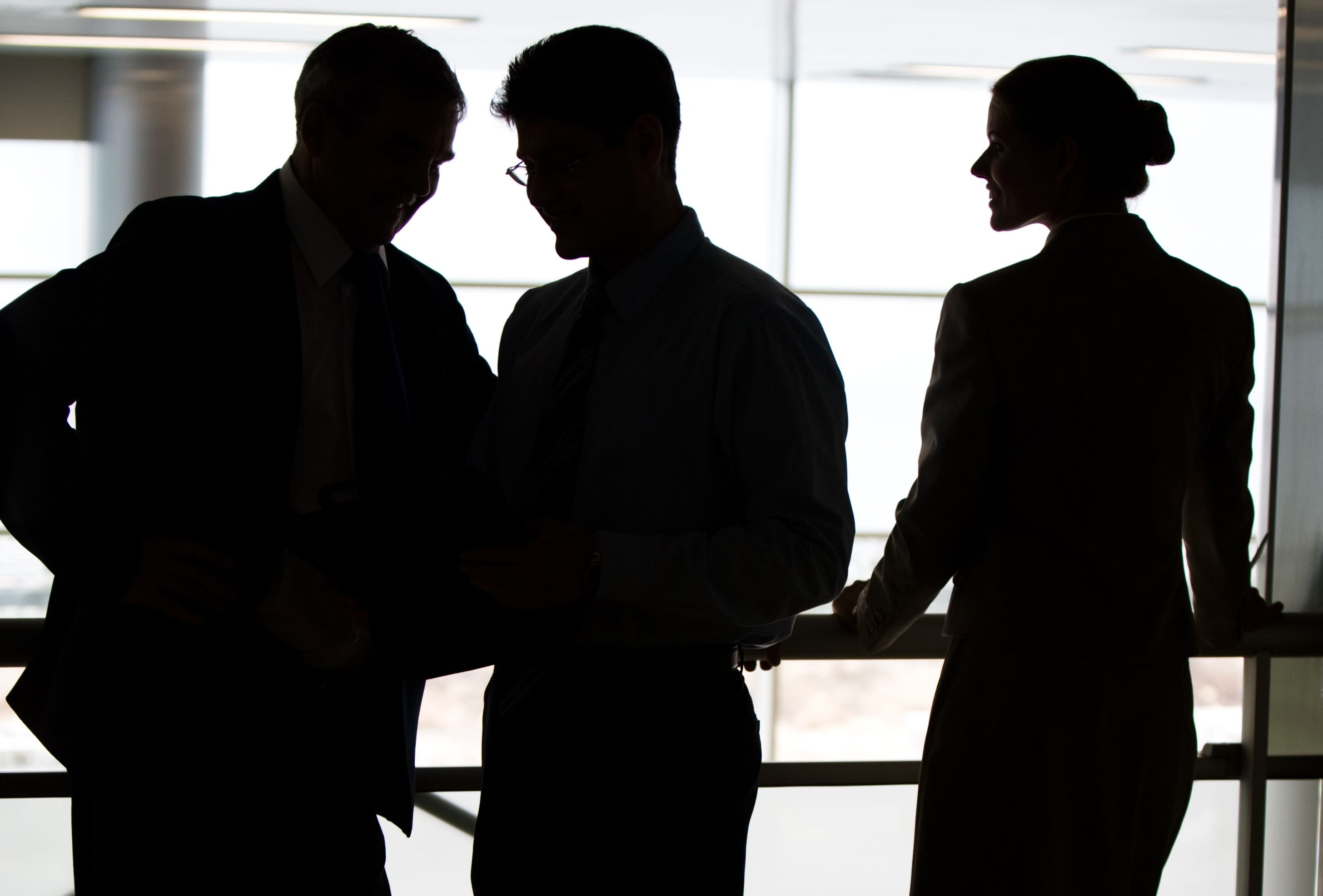 A man and two women in business dress stand on a balcony in an office.