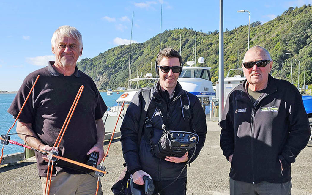 Radio Spectrum Management New Zealand investigator Mervyn Frericks (centre) with Kiwi Trust kiwi trackers Rick Boon and Ken Laurent investigate around the Whakatāne town wharf, searching for a rogue signal that is overriding a kiwi transmitter.