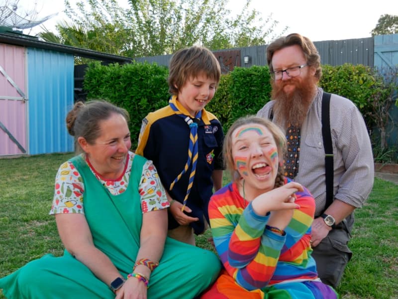 A family of four laugh on the grass.