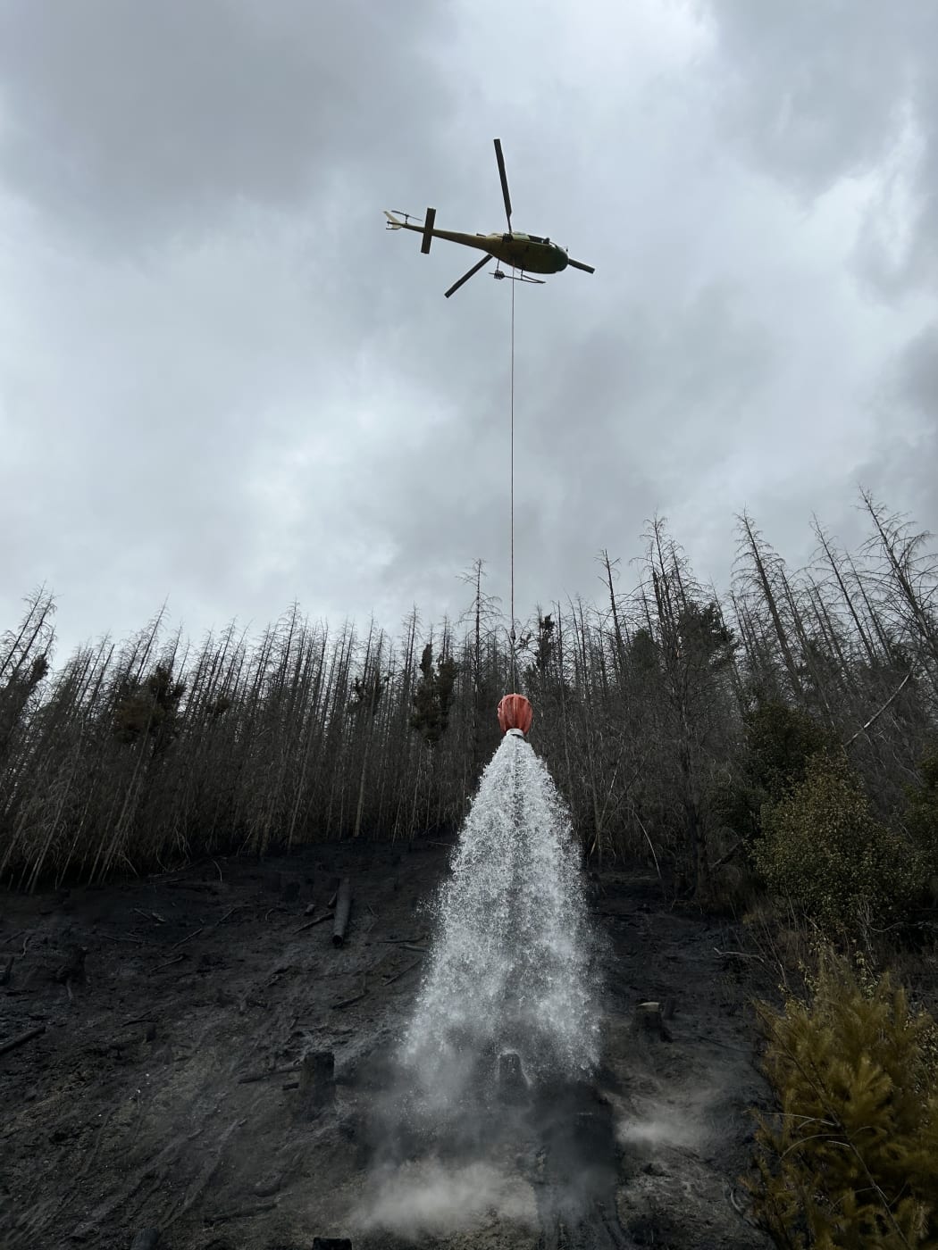 A helicopter water bombing a vegetation fire at Long Gully near Coronet Peak on 20 October 2023.