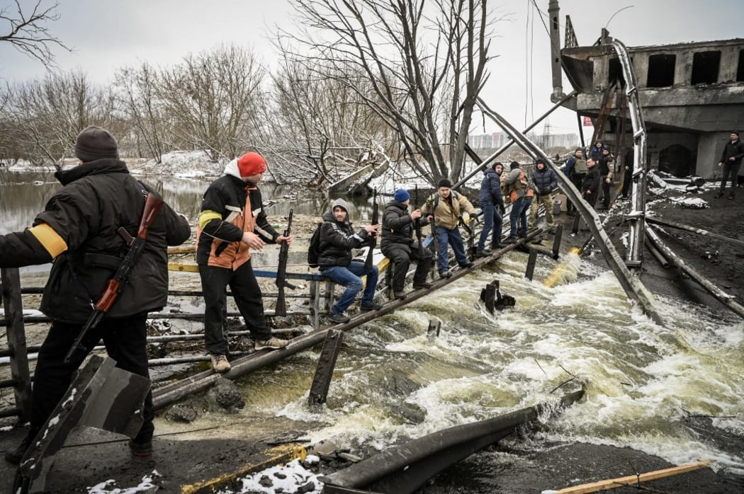 Members of a Ukrainian civil defence unit pass new assault rifles to the opposite side of a blown up bridge on Kyiv's northern front on 1 March, 2022.