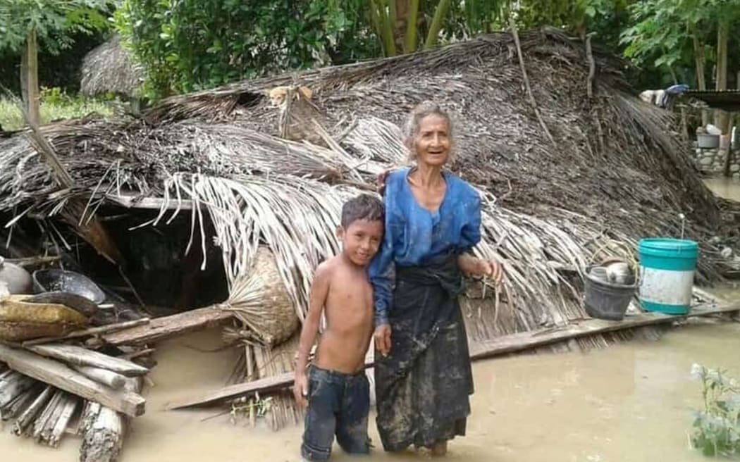 An elderly villager and her grandson stand in floodwaters in front of their damaged home in the village of Haitimuk in East Flores on April 4, 2021, after flash floods and landslides swept eastern Indonesia and neighbouring East Timor.