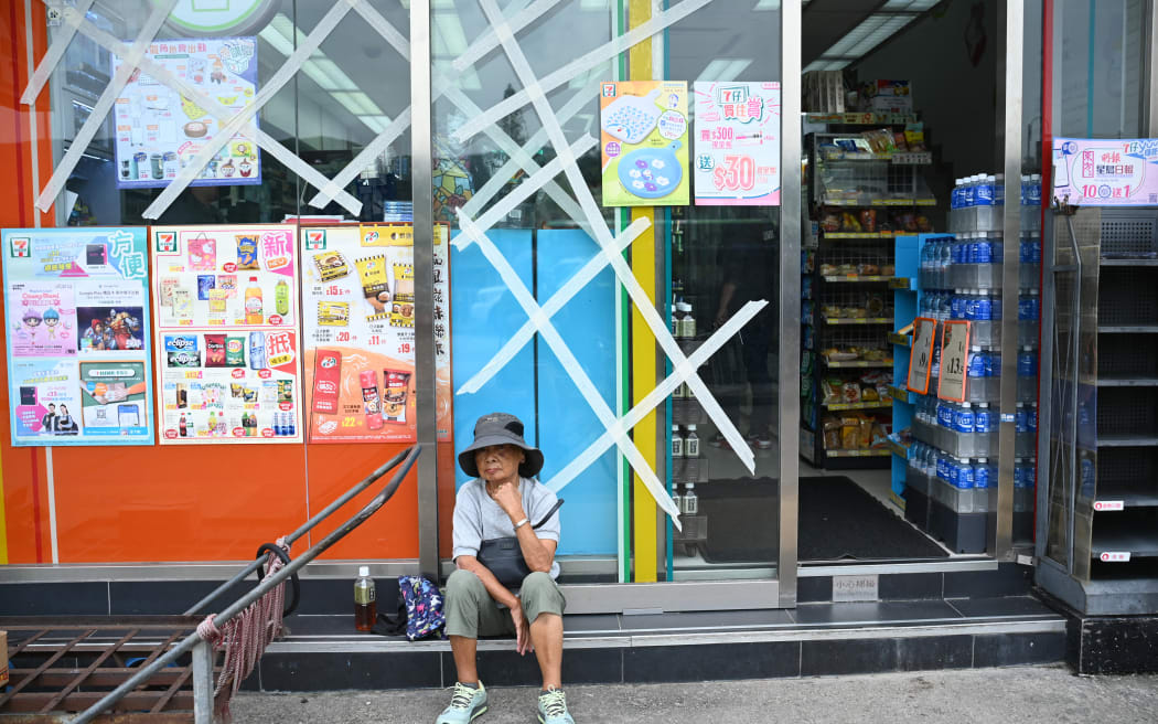 A woman sits outside a convenience store with windows taped up for protection on Lantau island in Hong Kong on September 1, 2023, hours before the expected arrival of Super Typhoon Saola. Hong Kong grounded flights, shut down its stock market and closed schools on September 1 as Super Typhoon Saola barrelled towards China's southern coast. (Photo by Peter PARKS / AFP)
