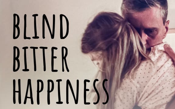 A father and daughter embrace in a somberly lit room, text over the top of the image reads "Blind Bitter Happiness". In the bottom left corner is the RNZ tohu badge.