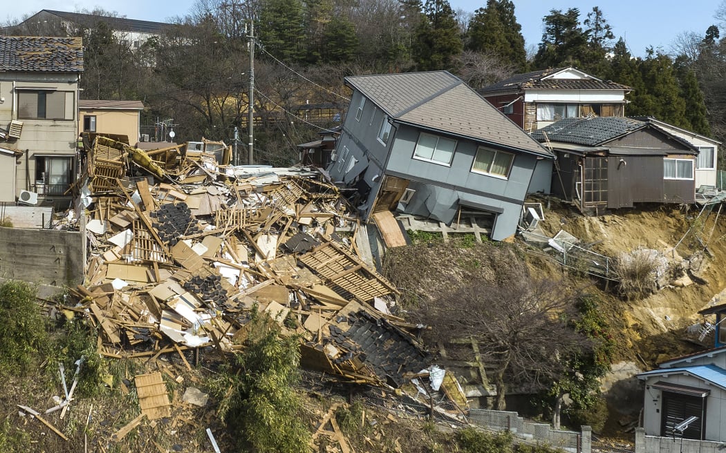 Damaged houses, including one totally collapsed (C), are pictured along a street in Wajima, Ishikawa prefecture on January 2, 2024, a day after a major 7.5 magnitude earthquake struck the Noto region in Ishikawa prefecture. Japanese rescuers battled against the clock and powerful aftershocks on January 2 to find survivors of a major earthquake that struck on New Year's Day, killing at least six people and leaving a trail of destruction. (Photo by Fred MERY / AFP)